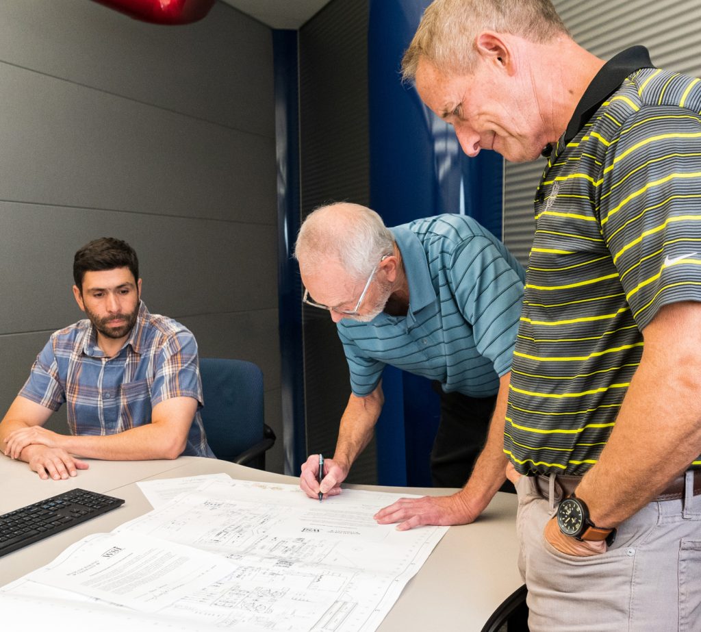 Three men reviewing engineering documents