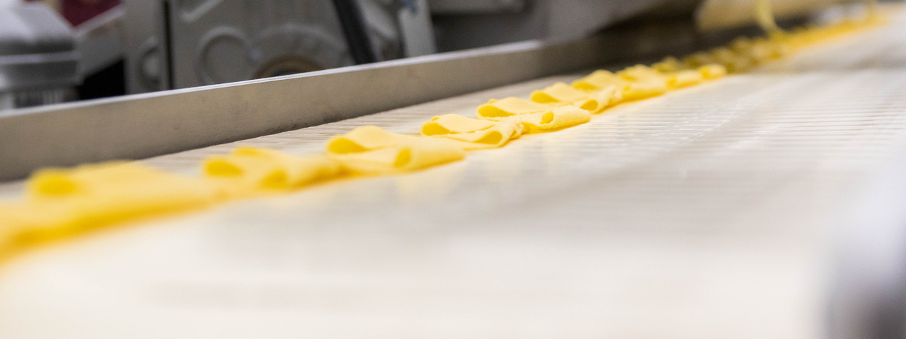 Hero image of a thinly rolled out dough on a conveyer belt 